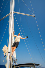 Man climbing the mast of a sailing yacht with full sails, captured from above near Croatia. Courage, freedom, yachting lifestyle and maritime exploration.