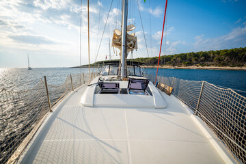 Fototapeta premium Sailing yacht anchored near uninhabited islands in Croatia, captured from the bow. Peaceful summer stopover and maritime leisure in a remote coastal area.