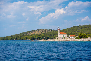 Stone lighthouse with red roof on the rocky coast of Hvar Island, Croatia, surrounded by pine trees...
