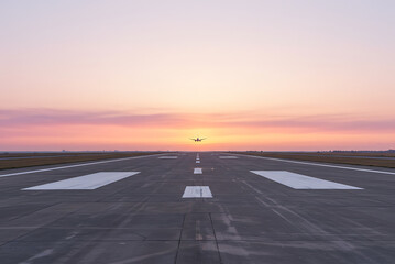 Naklejka premium Airplane approaching runway during colorful sunset with pink and orange sky airport landing