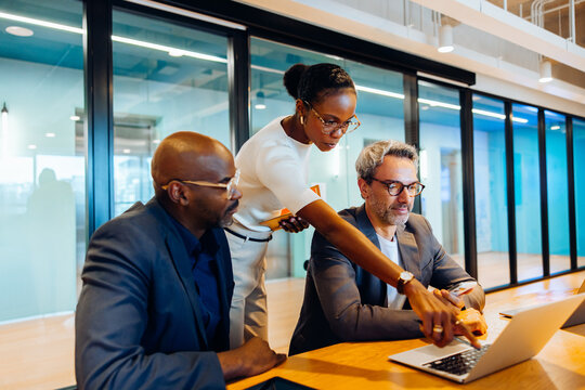 Three professionals discussing a project while using a laptop in a meeting