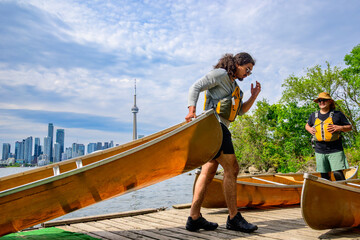 Active healthy lifestyle: a happy young man moves a canoe on a dock on the toronto Islands with the...