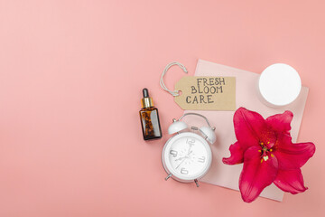 Skincare cosmetics concept with red lily on soft pink background, flat lay. Natural selfcare