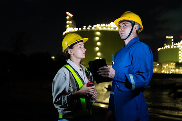 Male engineer and female engineer wearing helmets talking and working together at oil refinery site...