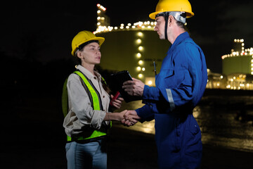 Male engineer and female engineer wearing helmets talking and working together at oil refinery site...