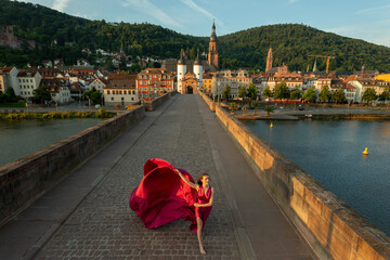 junge Frau in rotem Kleid, tanzt in der Morgensonne, über die alte Brücke in Heidelberg.