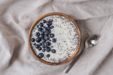 Wooden Bowl with Yogurt, Chia Seeds, and Fresh Blueberries on Linen Tablecloth. Healthy Breakfast and Clean Eating Concept