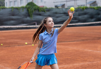 Girl practicing tennis on outdoor clay court with racket and tennis ball