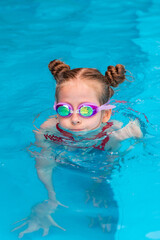 Cute little child girl learning to swim in the pool, wearing goggles. Childhood and development of children sport. Strengthening baby's health. Healthy activity for children. High quality photo