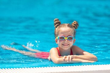 Cute little child girl wearing goggles, lying on the swimming poll side. Childhood and development of children sport. Strengthening baby's health. Healthy activity for children. High quality photo