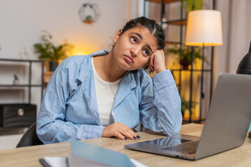 Sad Indian woman looks pensive thinks over life concerns or unrequited love, suffers from unfair situation. Problem, break up, depressed feeling bad, burnout. Girl at home office at table. Lifestyle.
