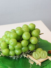 A bunch of fresh grapes on a rustic wooden plate decorated with green palm leaves, tropical and natural still life composition, close-up.