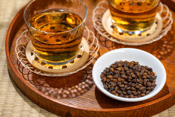 白い器に入った丸粒の大麦と後ろに並ぶ麦茶のグラス