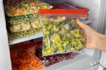 Female hands retrieving frozen broccoli from freezer. Plastic bags with different frozen vegetables and berries in refrigerator.  Winter supply food in zip bags, preserving nutrients.