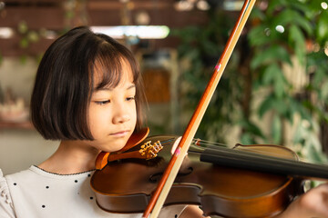 Asian girl passionately plays the violin, demonstrating focus and dedication during a music lesson. Her precise movements and deep concentration highlight her growing talent as a young musician.