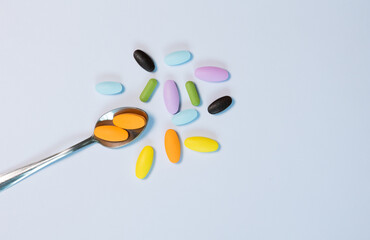 Top-view colorful pills and multivitamins with spoon on white background. Lay flat composition with copy space shows healthcare, daily supplement, and pharmaceutical lifestyle in clean, minimal style.