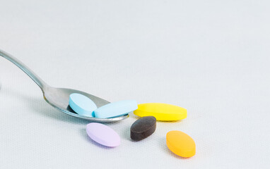 Colorful tablets and pills resting on a metal spoon, arranged on a clean white background with copy space. Close-up concept of daily medication, vitamin intake, and modern healthcare lifestyle.
