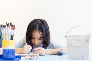 Young Asian girl focuses on painting a clay object, with her hand and brush with selective focus shows creativity and calm concentration for kid learning activity  via art and development in child.