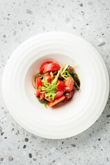 Close-up of fresh salad with tomatoes, olives, red onions, and leafy greens in a white bowl, ideal for concepts of healthy eating, vegan food, and organic nutrition.