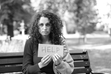 Homeless woman with sign Help on bench in park, space for text. Black and white effect