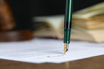 Signing notary document with fountain pen at table against black background, closeup