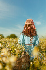 Back view girl in blue linen dress and fashionable pink crochet beanie sits in daisy field in summer day