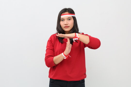 Indonesian woman with red and white ribbon celebrating Indonesian independence day, standing while showing hand gesture of time up, warning or prohibition, isolated on white background.