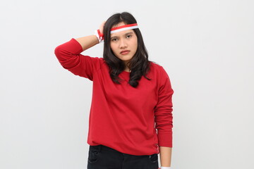 Confused Indonesian woman with red and white ribbon celebrating Indonesian independence day, standing scratching head looking at camera, isolated on white background.