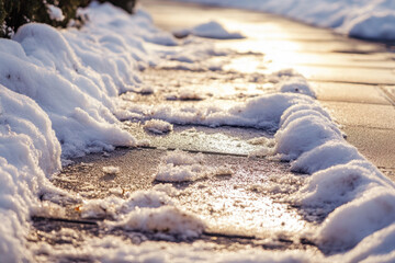 Paved path is covered with fresh snow and some melting ice, reflecting the warm golden sunlight of a crisp winter day outdoors.