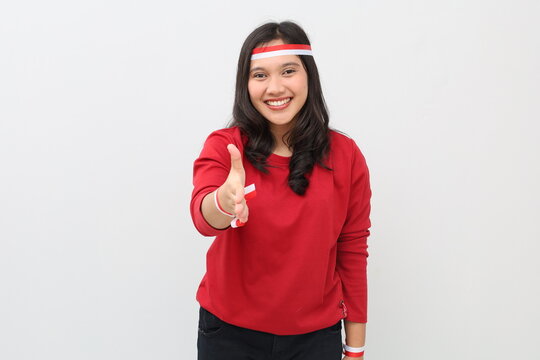 Indonesian woman wearing red and white ribbon celebrating Indonesian independence day smiling while standing extending hand in handshake gesture looking at camera, isolated on white background.