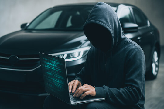 Cyber Criminal and Hacked Vehicle: An image portrays a hooded individual focused intensely on a laptop, implying a potential cybercrime, set against the backdrop of a parked vehicle.