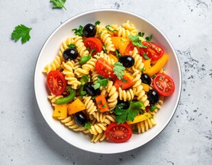 Fresh and colorful pasta salad featuring spiral pasta, red tomatoes, black olives, and bright bell peppers rests in a white serving bowl.