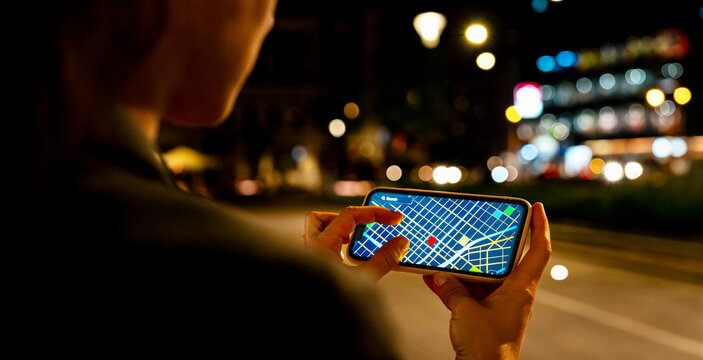 Woman using digital map app on smartphone while walking in city at night