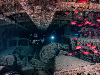 Scuba divers explore an old sunken engine room surrounded by red reef fish underwater in Red Sea