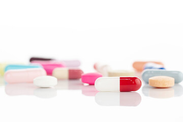 Assortment of colorful medicine pills and capsules on a reflective white background. Concept of...