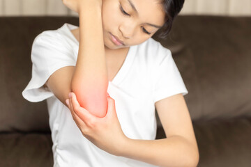 Asian child with elbow pain and injury. Unhappy young girl holding painful arm with red inflammation, a symptom of joint ache, trauma, or dermatitis.