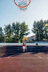 two children playing basketball on empty court with school in background, visible copy space, concept of youth movement, community fitness, education promo
