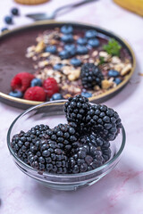 Clear glass bowl filled with vibrant blueberries, on a marble table with natural light that enhances their colors