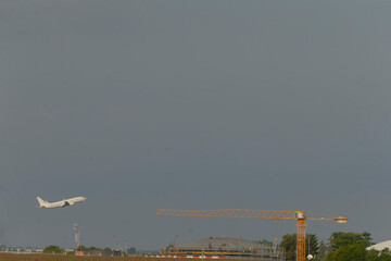 A plane is soaring through the sky high above a construction site where a large crane stands prominently in the foreground, showcasing modern engineering marvels