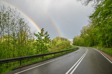 wet road from the rain, cloudy sky, and rainbow in Mazury