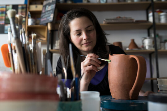Potter painting unfinished vase in her workshop