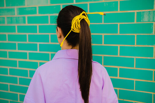 Ponytail of young woman tied with yellow cable in front of wall