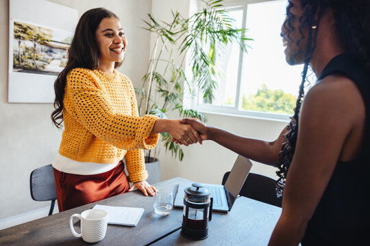 Two young women shaking hands in a modern architecture firm office