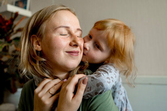Daughter embracing mother from behind and kissing her on cheek at home
