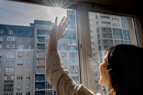 Woman shielding eyes looking at bright sun through window
