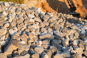 pile of gray and white rocks in construction site bathed in warm sunlight with earthmover in background illuminating textures and shadows on stones, color, manual, ground, environment, worksite