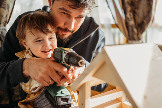 Father assisting son building up birdhouse at home