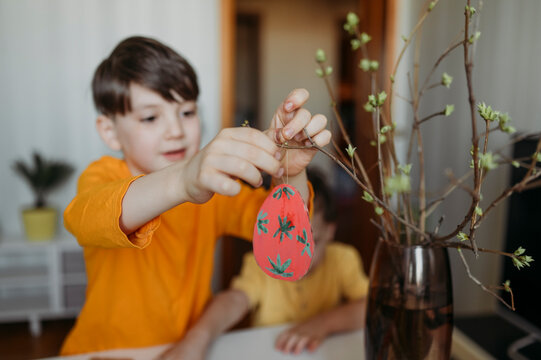 Boy decorating cardboard Easter eggs on twig
