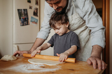 Father helping son to roll dough in kitchen at home