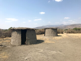 Traditional Maasai huts in a remote, arid African savanna under a vast, cloudless sky, symbolizing traditional nomadic life in East Africa.